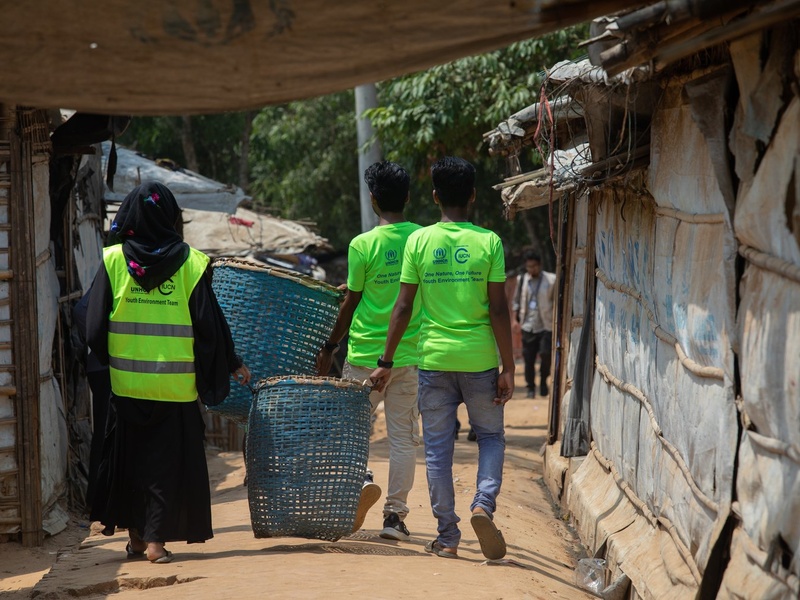 Young Rohingya refugees carry bamboo bins through a camp.