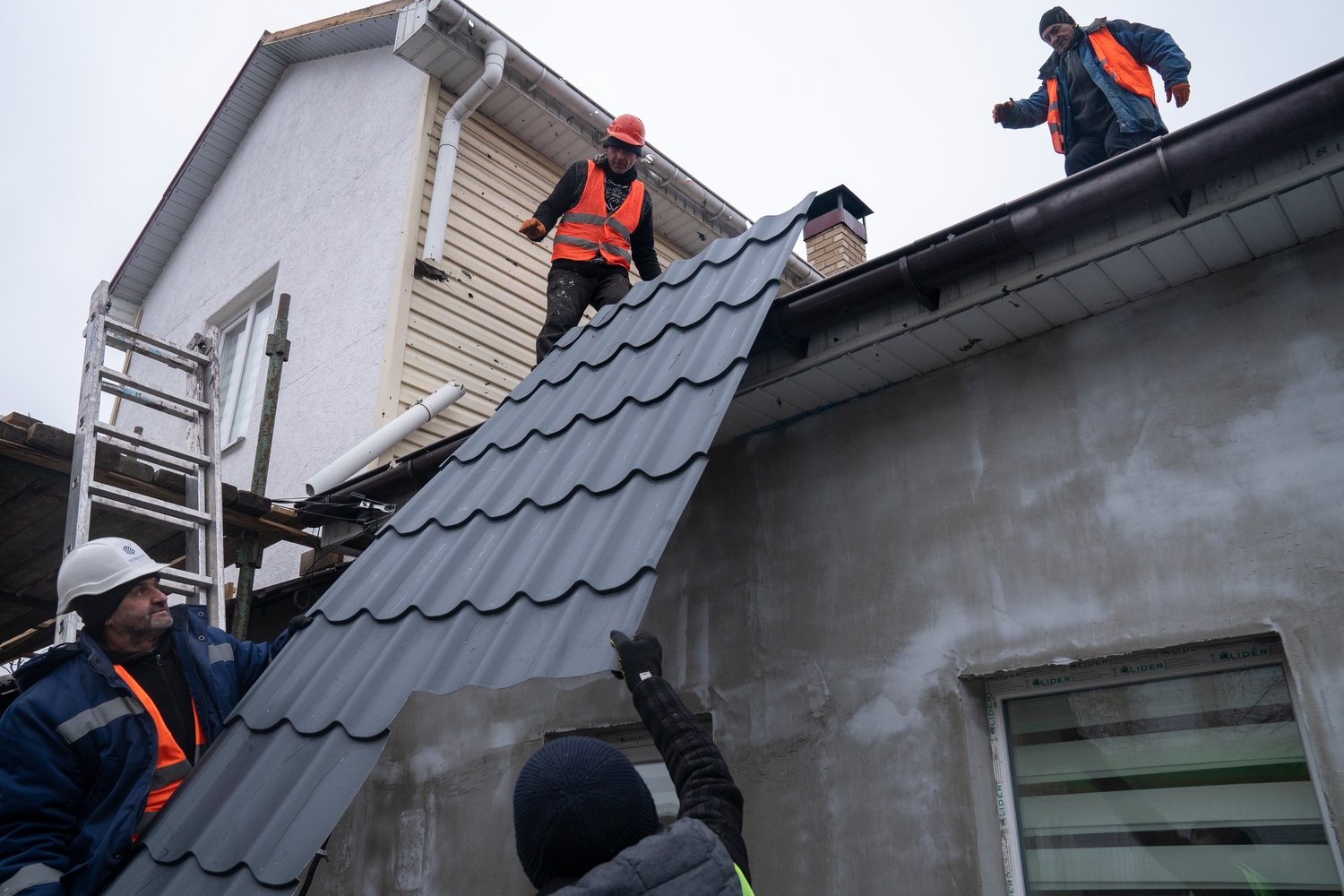 Workmen lift a new section of roof into place on a house in Ukraine