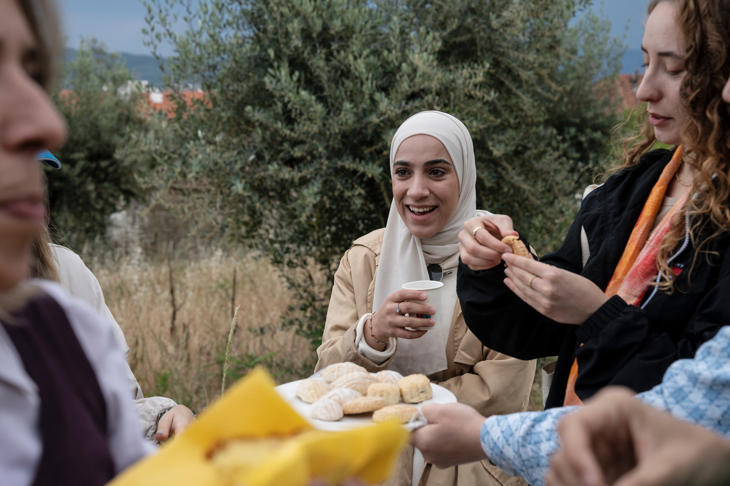A young woman laughs as food is passed around at a picnic.