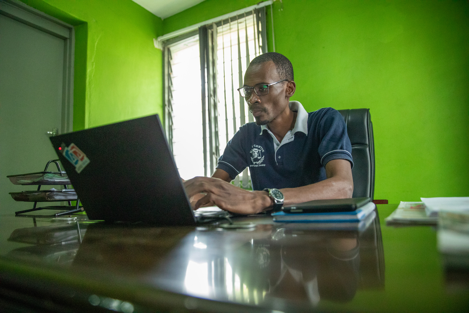 A man sits at a desk in an office, working on a laptop.