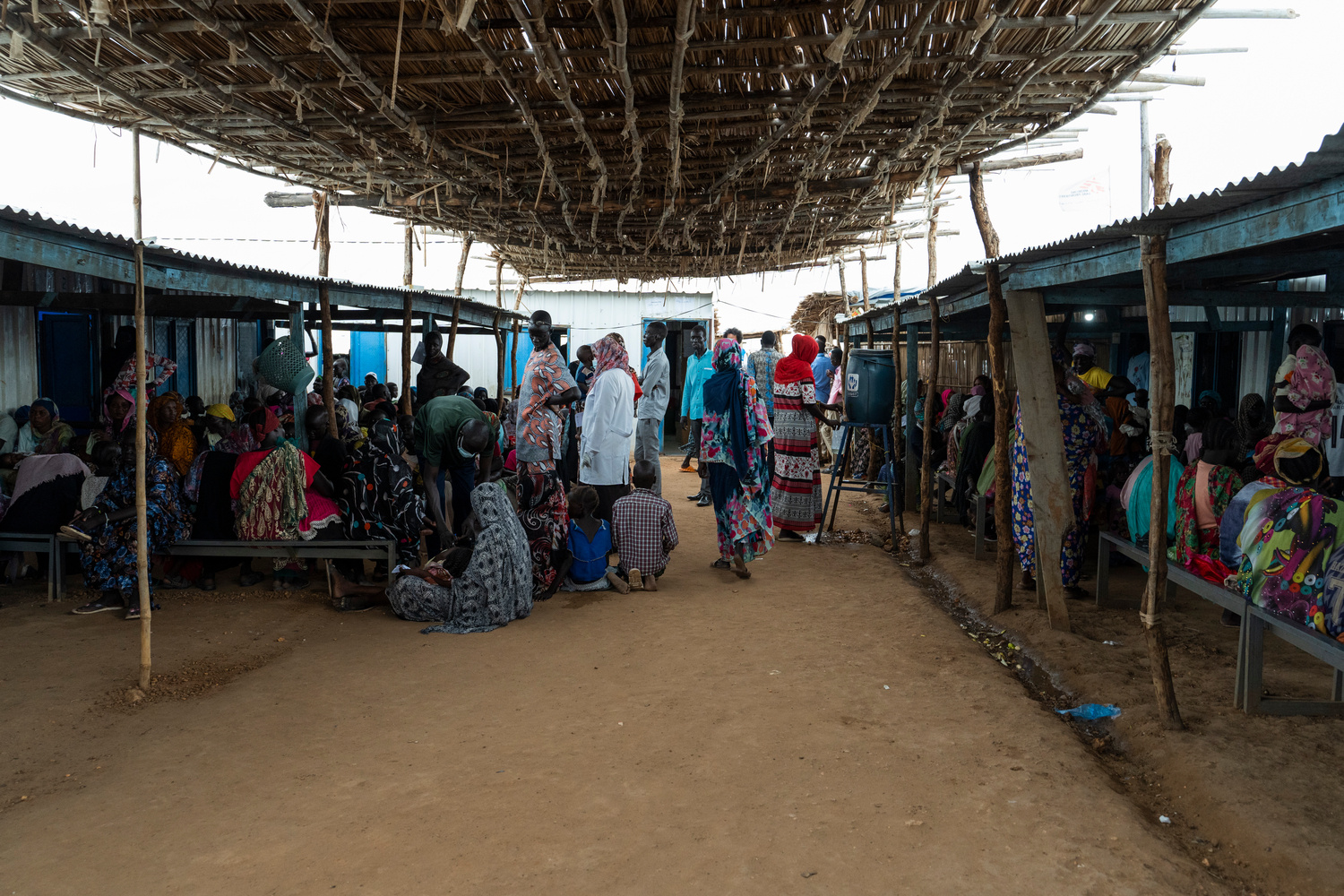 A shaded waiting area full of people outside a health clinic.