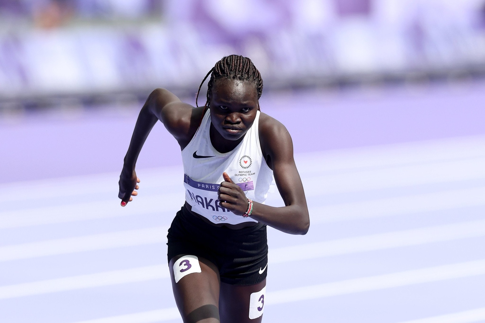 A woman wearing a white vest and black shorts runs on a track