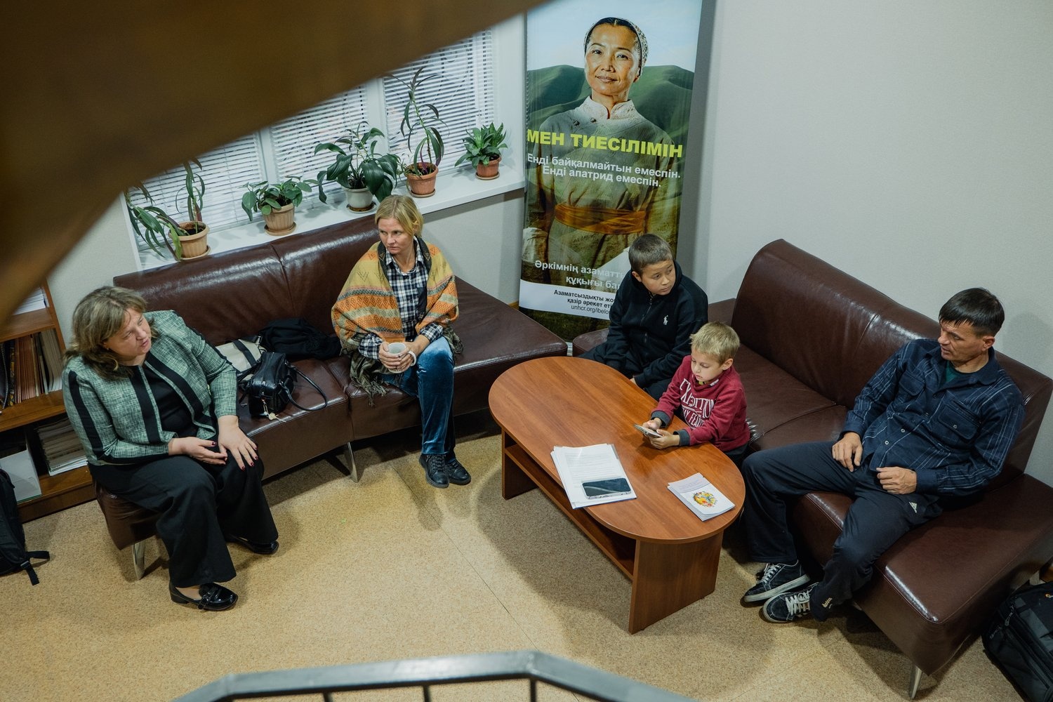 A man and a woman and two boys sit on leather couches talking to another woman.