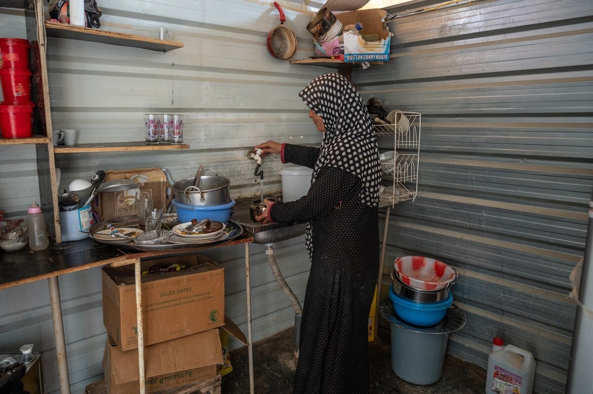 A woman stands inside the kitchen of her shelter as she washes dishes.