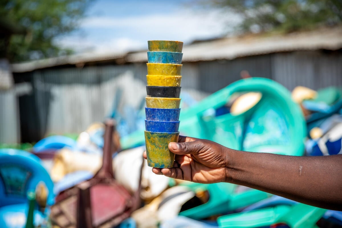 A hand holds up a stack of colourful cups made from recycled plastic waste
