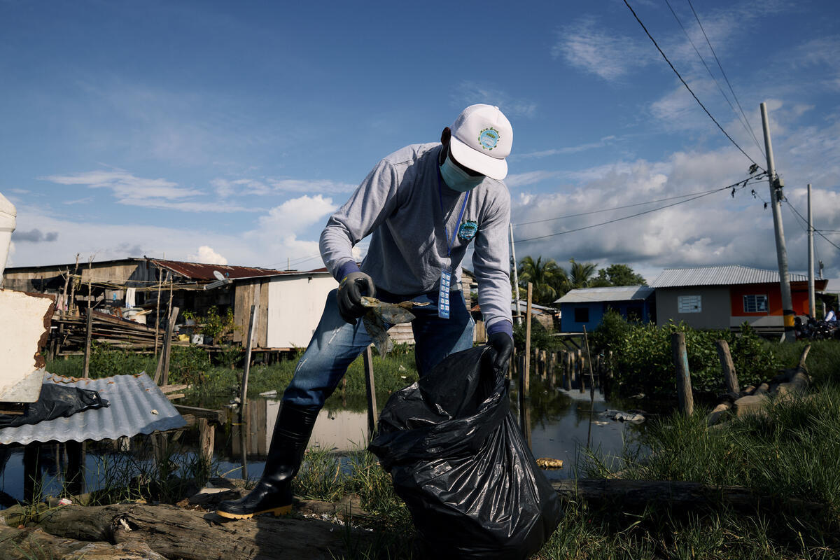 A man wearing a face mask and gloves puts rubbish into a black bin bag.