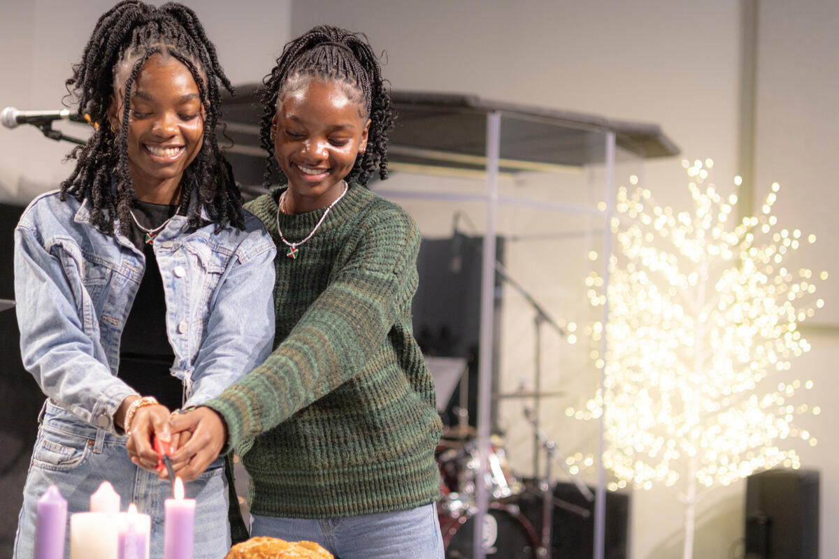 Two young sisters smile as they light a candle together.