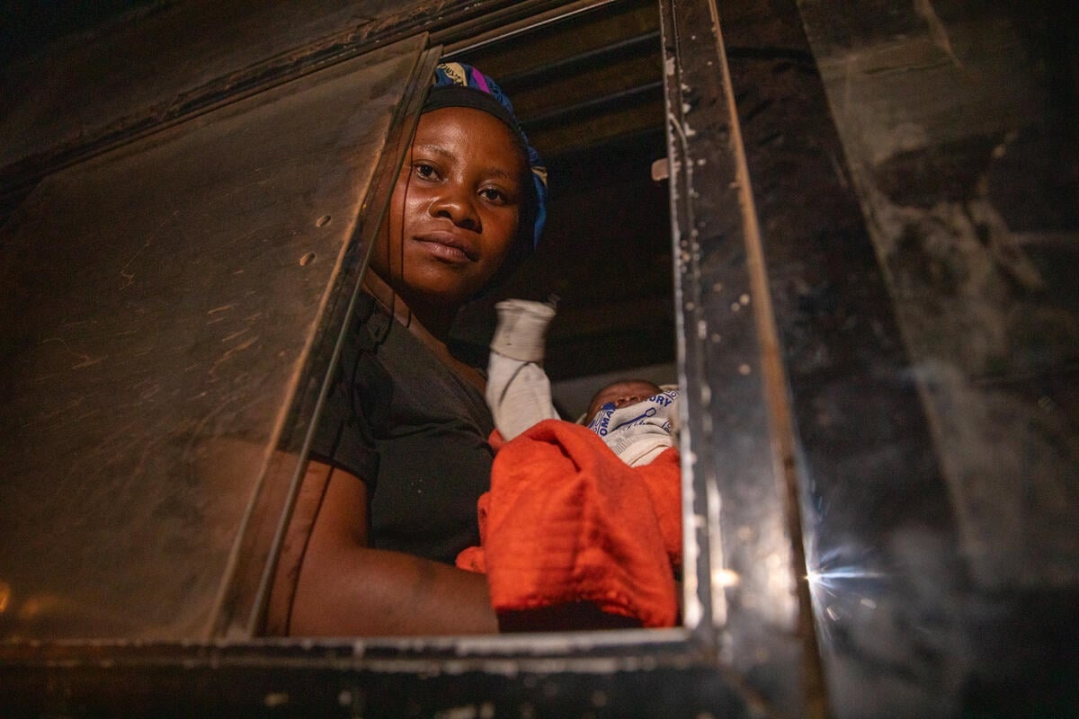 A woman looks through the window of a bus as she holds her child.