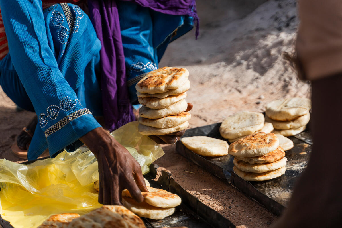A woman picks up small rounds of bread to sell to a customer.