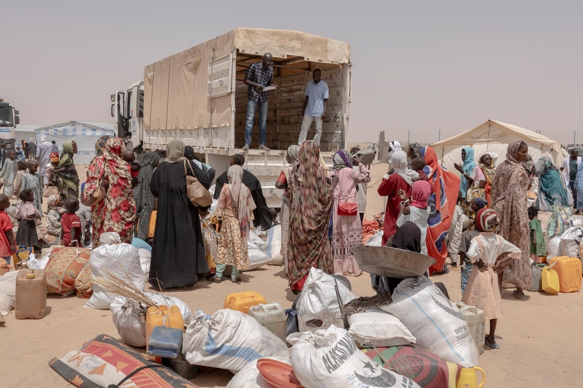 A group of people gather behind an empty truck with their belongings spead around them on the ground.