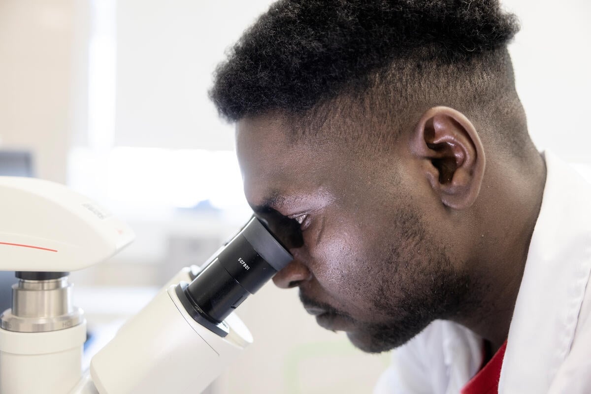 A man wearing a lab coat looks into a microscope inside a laboratory