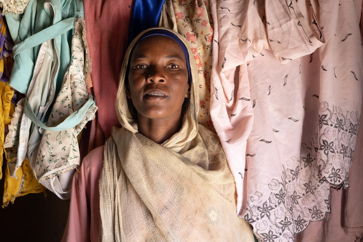 A woman stands in a room with garments hanging on the wall behind her