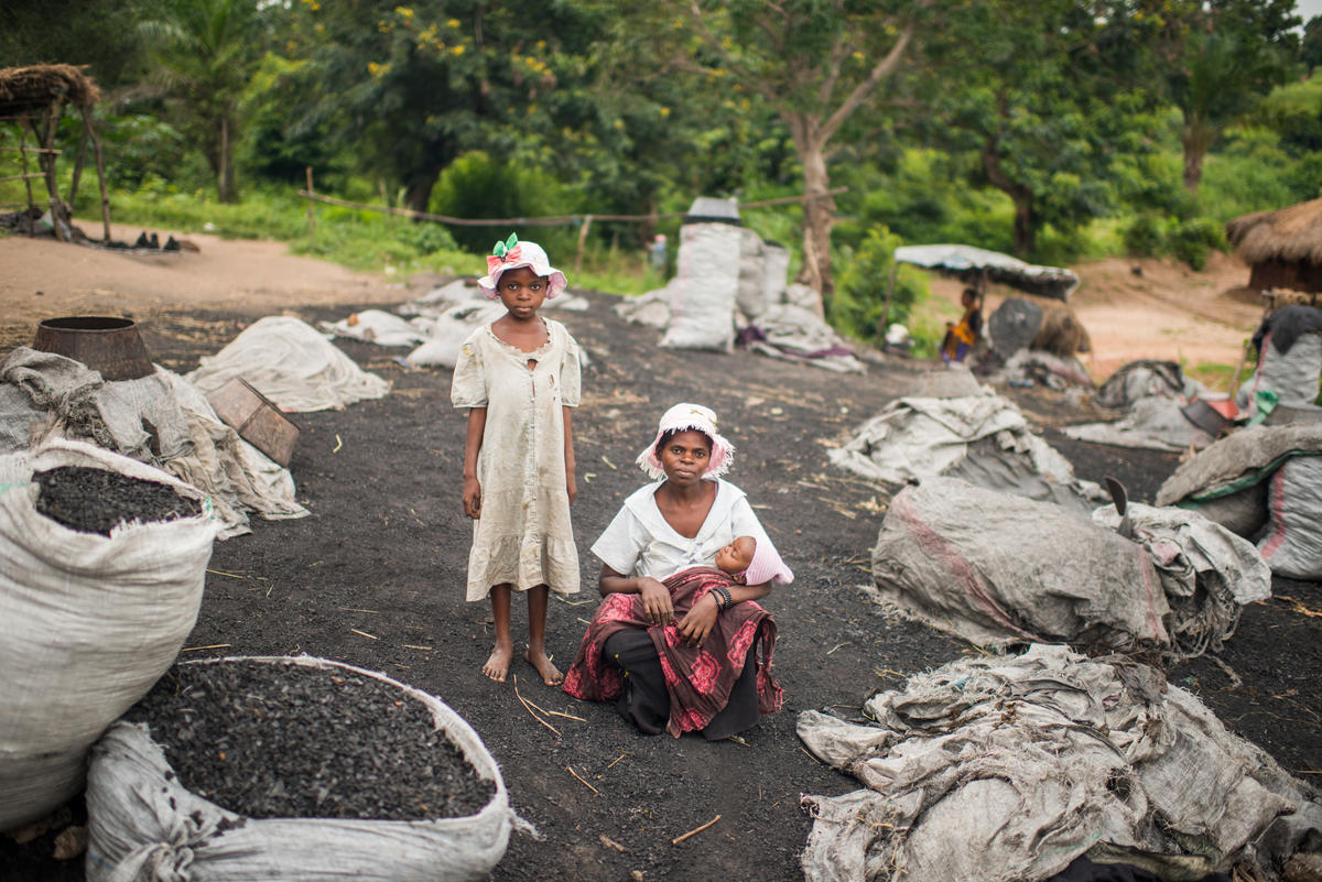 Surrounded by bags of coal they have packed, a displaced Congolese woman poses for a photo with her two children.