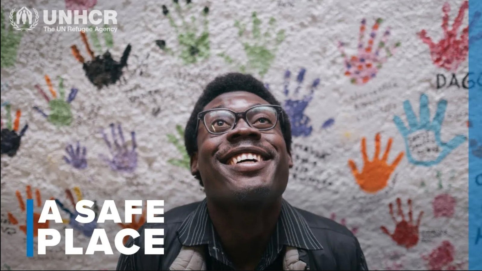 A portrait of a man in front of a wall covered in colourful handprints.