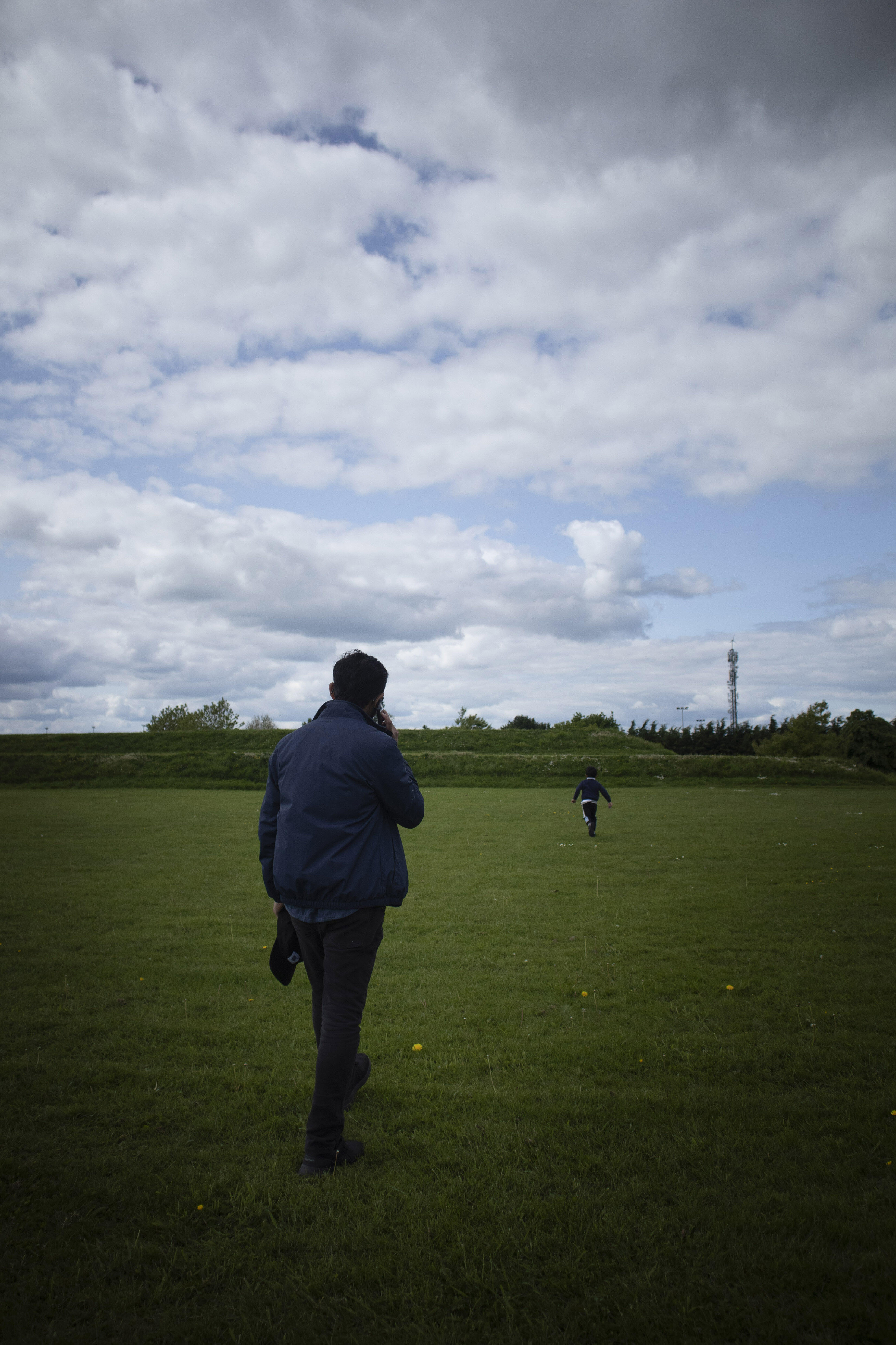 A man is on the phone in a park, a child runs ahead of him.