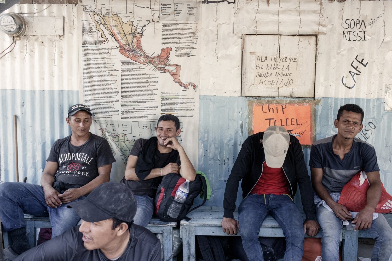 Men sit on a bench in front of a map of Mexico.