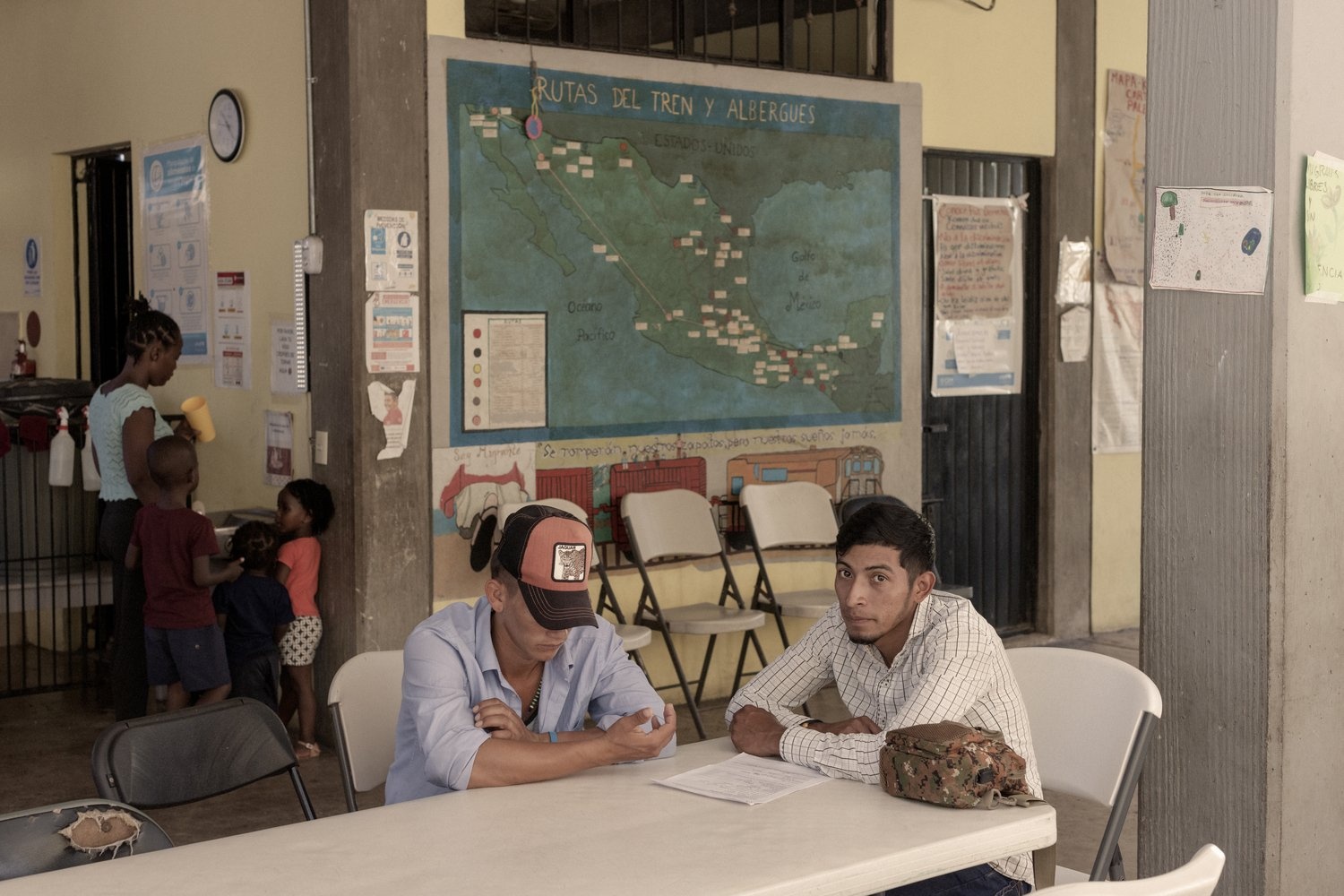 Two men sit at a table. Behind them is a map of Mexico.