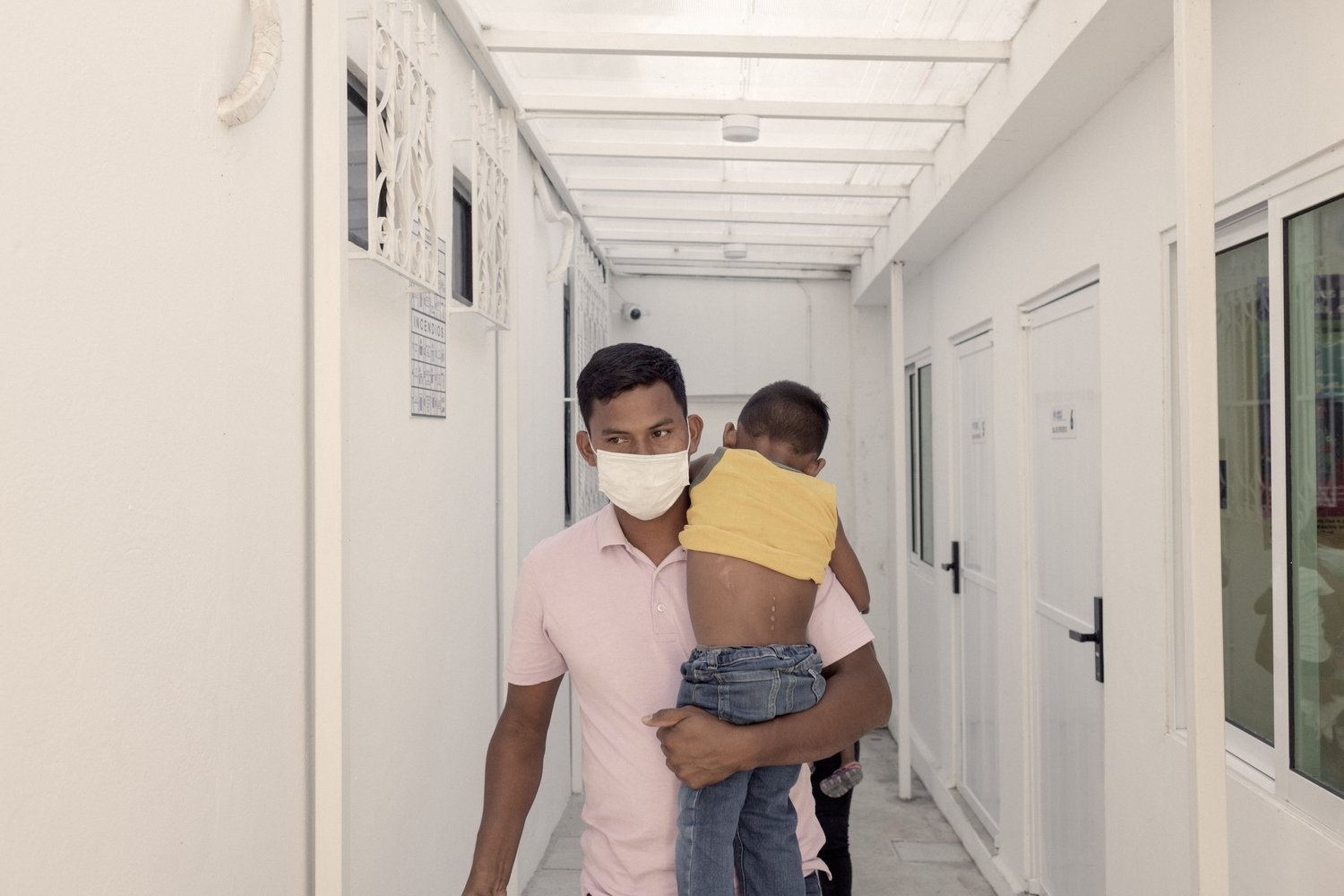A man wearing a mask walks down a corridor carrying a young boy.