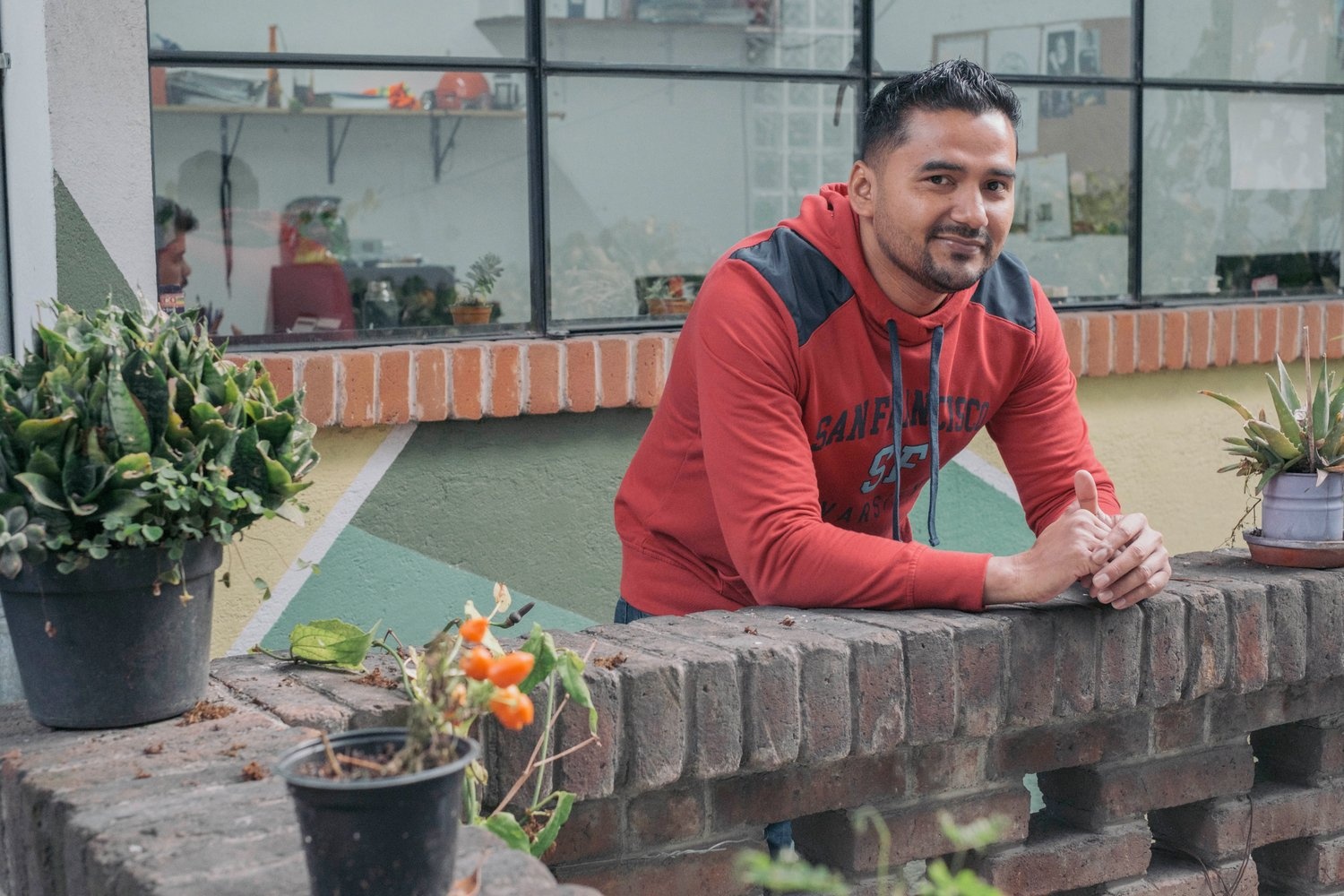 A man in a red hoodie leans on a low brick wall.