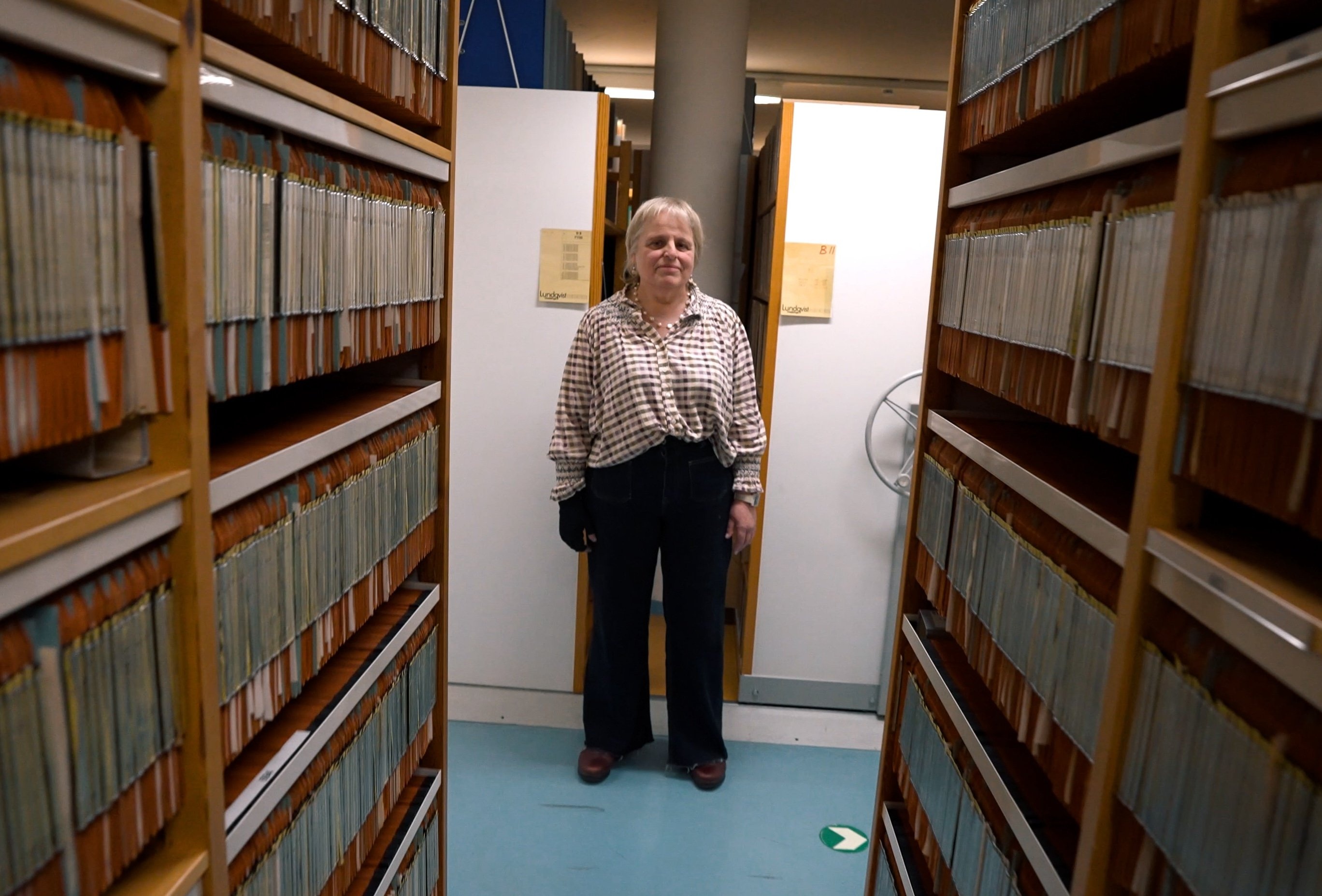 A woman stands at the end of a row of archive shelves.