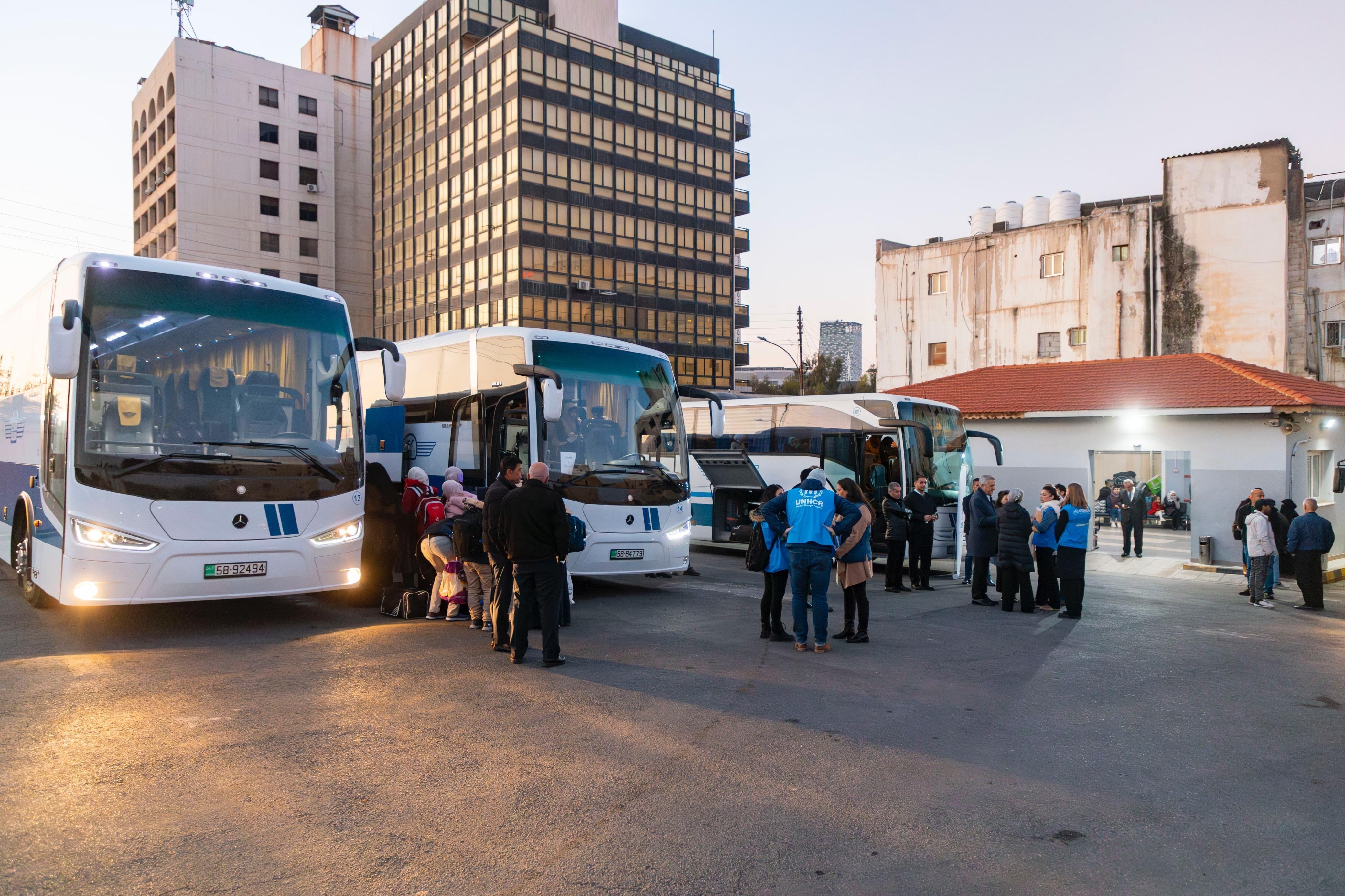 Families board one of three buses in a lot while groups of people stand nearby