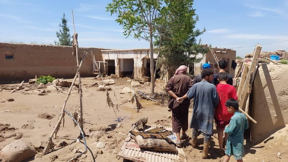 A family walks through mud near flood damaged homes