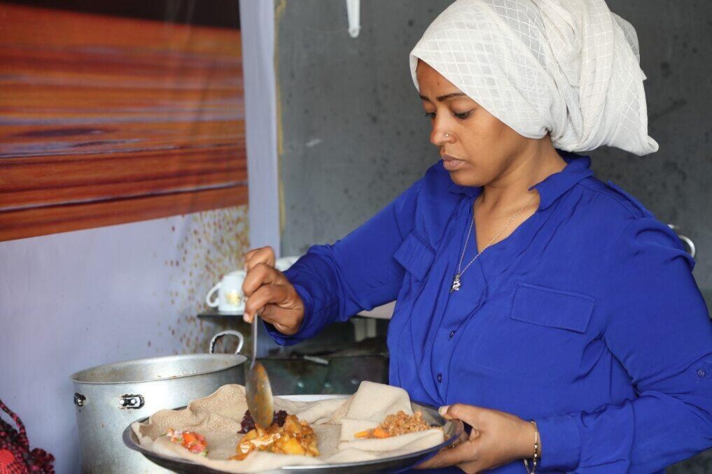 A woman spoons food from a saucepan onto a plated flatbread