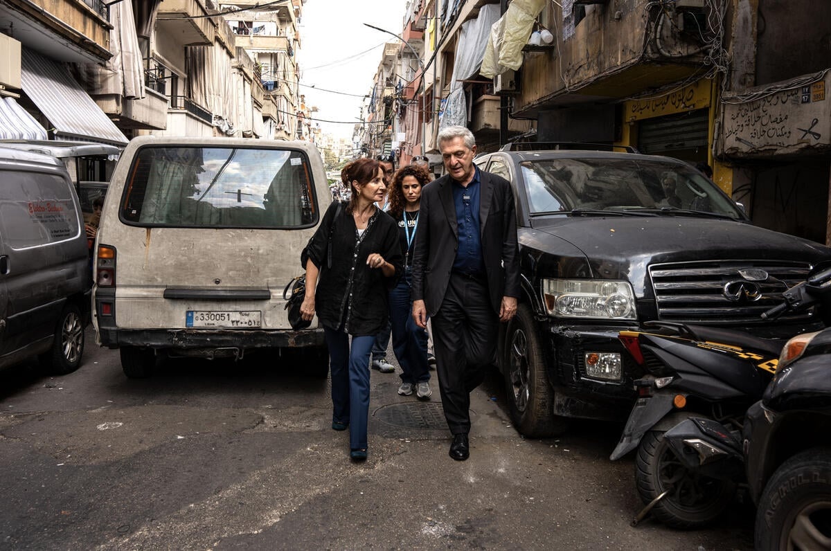 A group of three people walk between parked cars in a narrow street in Beirut.