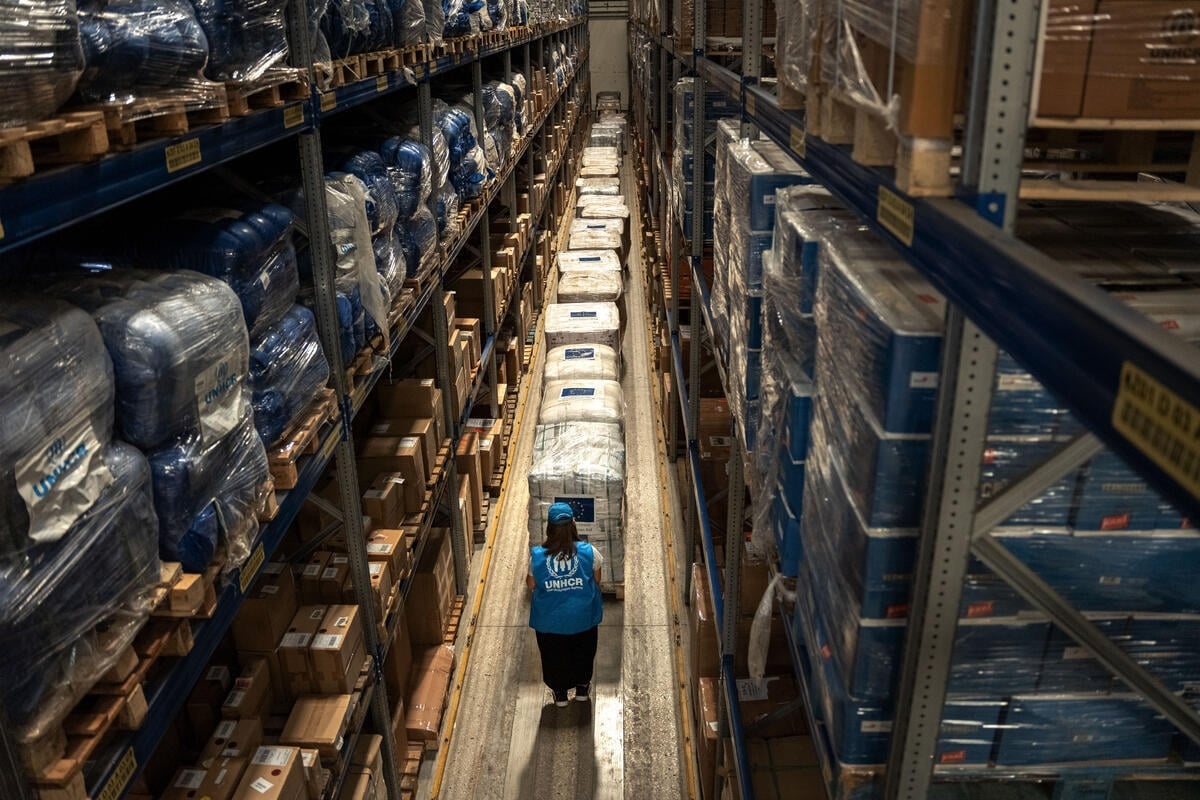 A UNHCR worker in a warehouse surrounded by pallets of humanitarian aid.