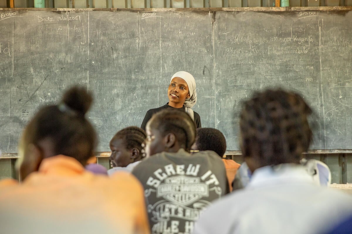 A young woman stands in front of a blackboard addressing a class of other young women.