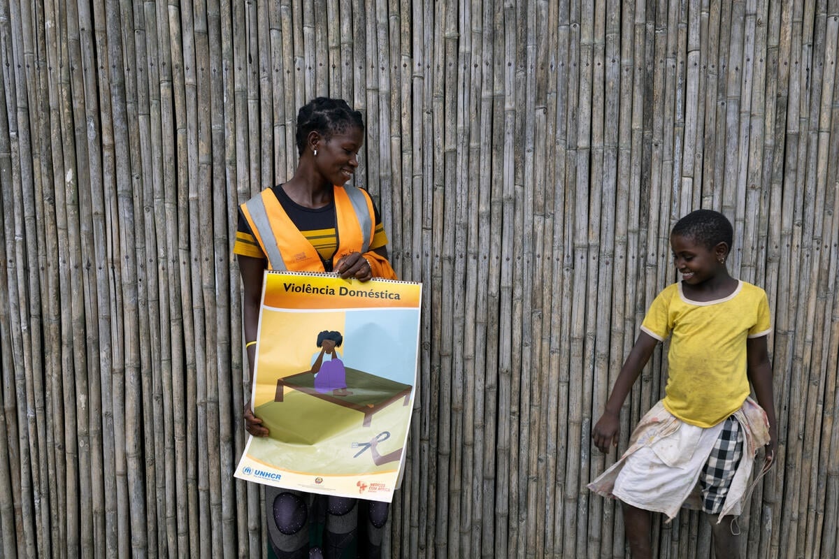 A young woman holding a poster about gender-based violence smiles at a girl in a yellow t-shirt.