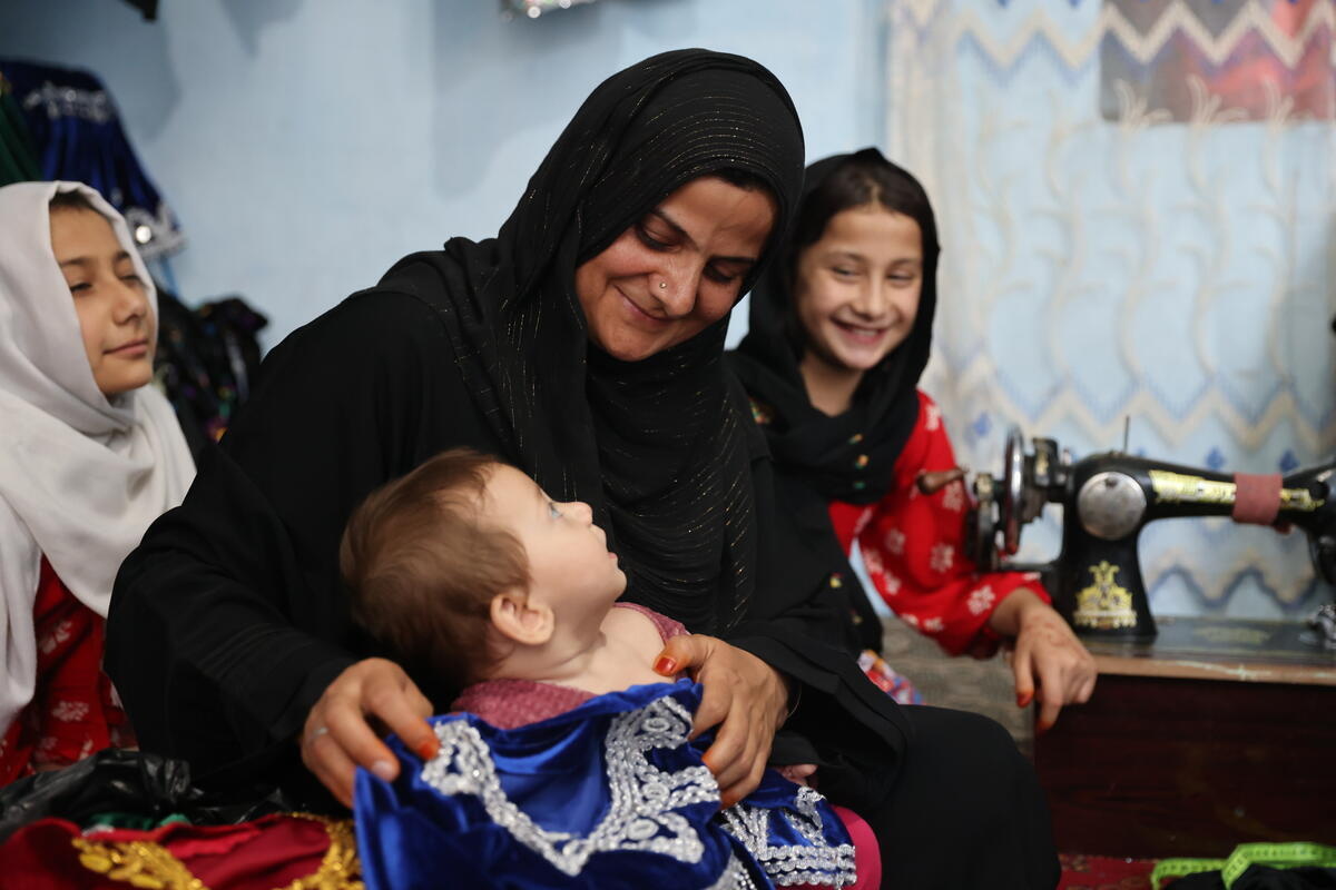 A woman, surrounded by three children, sits in a room with a sewing machine in the background.