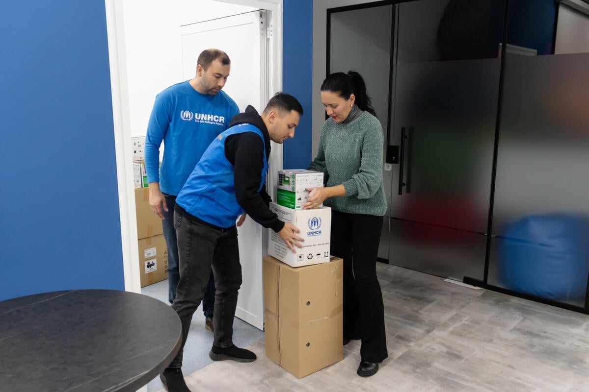 A woman receives boxes of aid supplies from two UNHCR staff members.