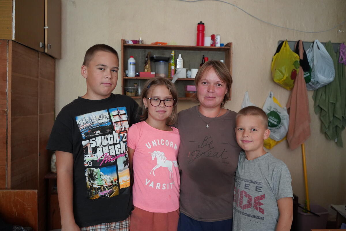A mother and her three children stand arm in arm inside their home
