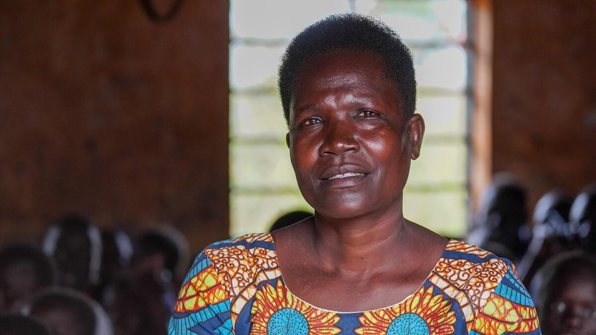 A woman in a colourful dress stands in a classroom full of students in front of a window