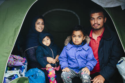 A small family of asylum-seekers smile from inside their tent at an improvised camp in Greece. 