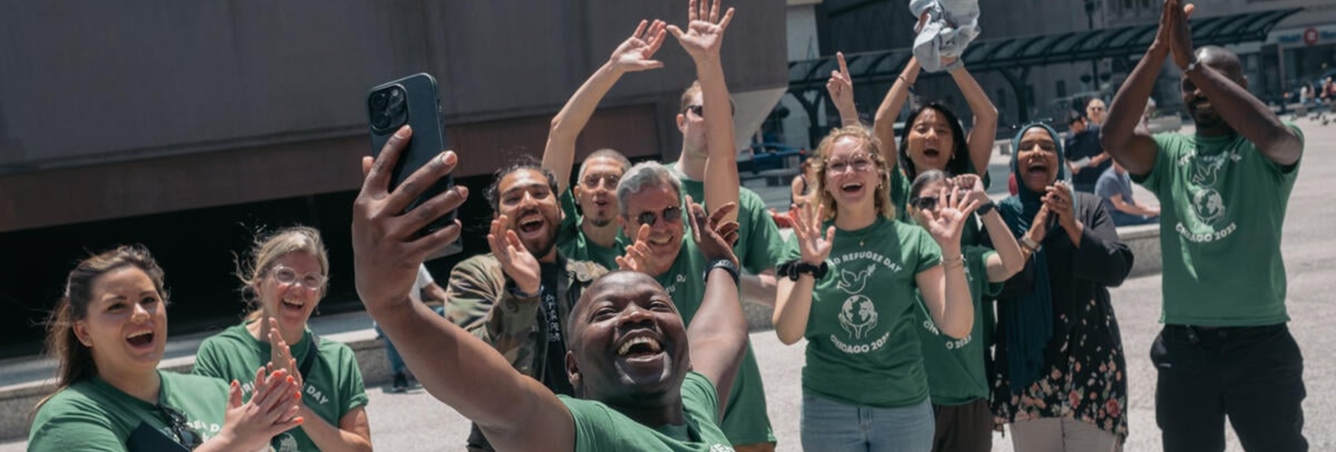 A group of smiling, cheering people take a selfie in Chicago at World Refugee Day celebrations