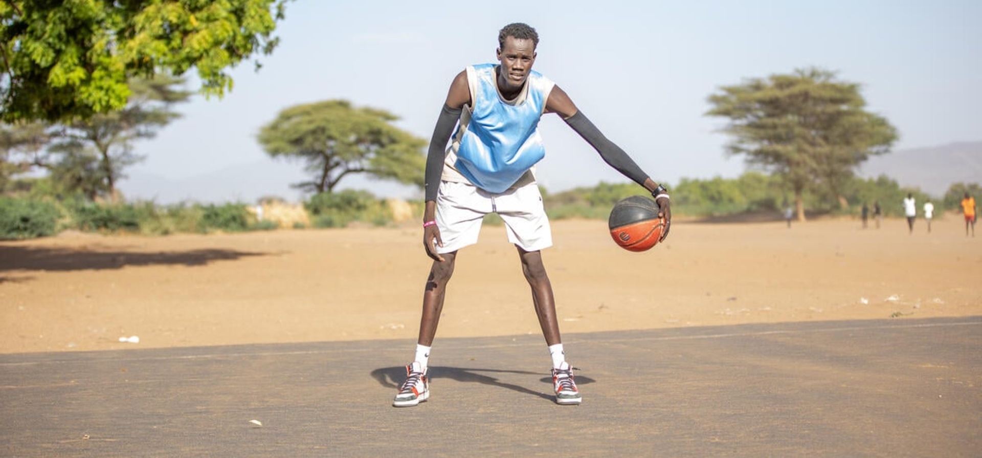  South Sudanese refugee Lich Gatkoi dribbles a basketball on an outdoor court.