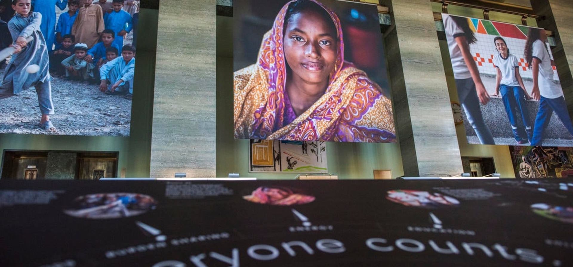 A photo exhibition at the United Nations, featuring a large image of a smiling woman in a pink and yellow headscarf.
