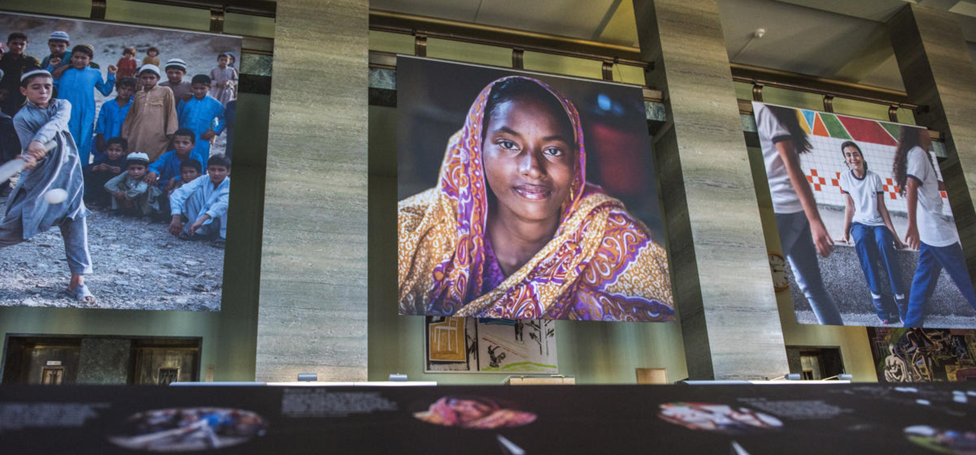 A photo exhibition at the United Nations, featuring a large image of a smiling woman in a pink and yellow headscarf.