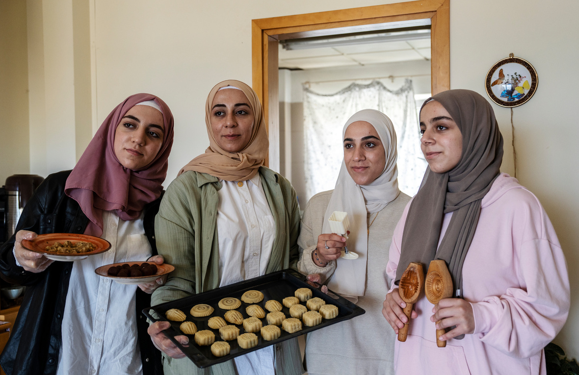 Four young women wearing headscarves hold up a tray of cookies.