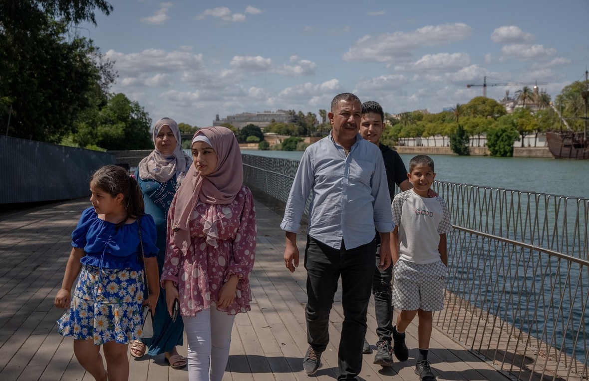 A couple and four children walk along a boardwalk next to a river.