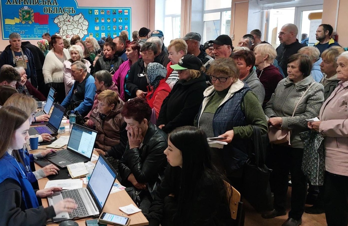 A large group of people are registered on computers by five UNHCR staff at a busy transit centre