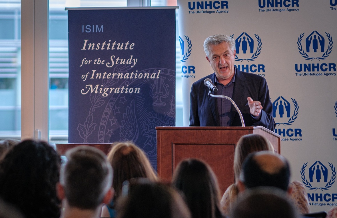 Filippo Grandi speaks from a podium in front of a UNHCR banner and next to a banner which says 'Institute for the Study of International Migration'