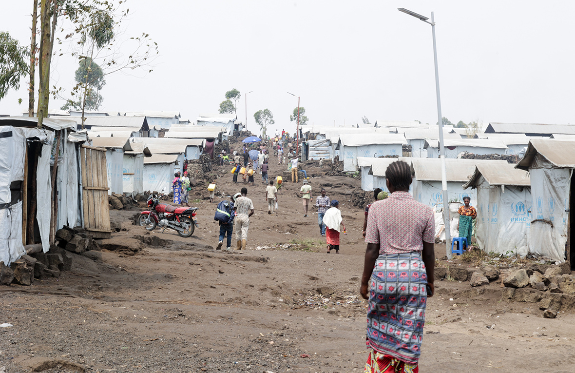 People in ones and twos walk over the undulating dry ground through a camp for internally displaced people 