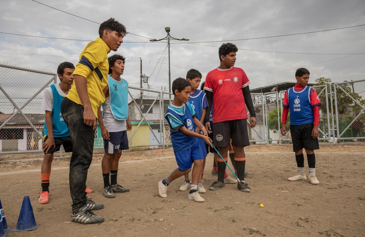 A young boy hits a yellow ball with a golf club as a group of children look on
