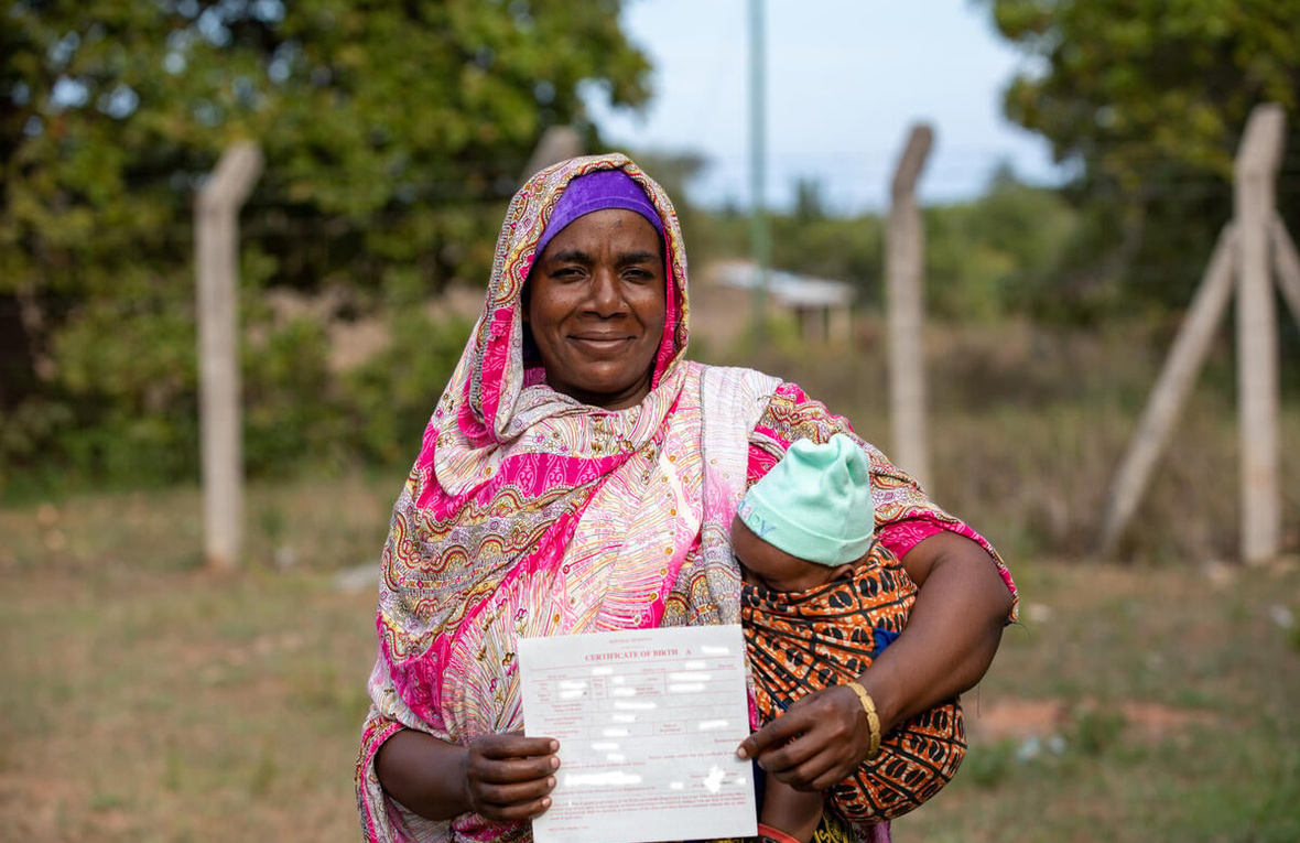 A Pemba woman from Kenya smiles while holding a baby in her arms, proudly displaying a document.