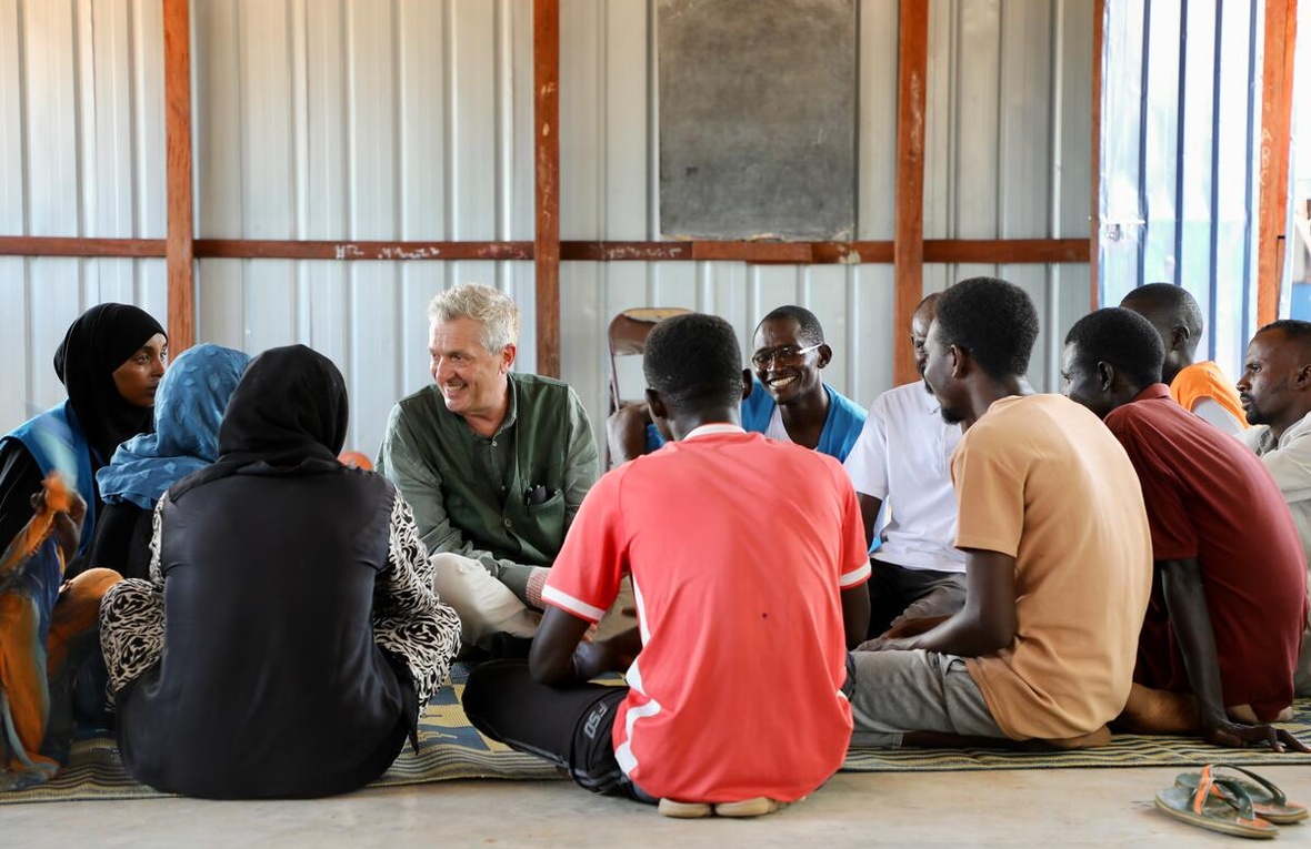 High Commissioner Filippo Grandi sits on the ground with a group of young Sudanese refugees