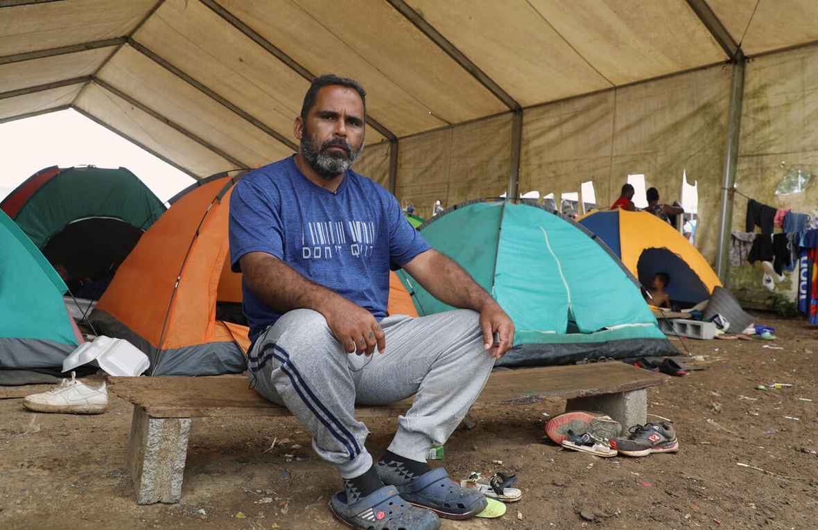 A man sits on a low bench in front of some tents.