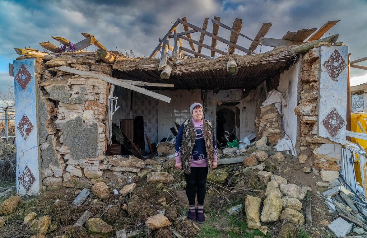 A woman stands near the remains of her house